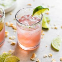 guava margarita on the rocks with a coconut lime salted glass rim and a lime wedge
