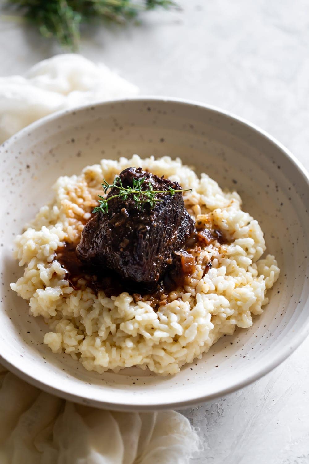 red wine braised short ribs on top of Parmesan risotto in a ceramic bowl with thyme