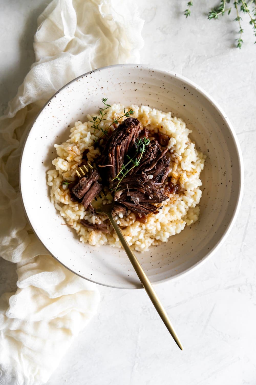 red wine braised short ribs on top of risotto with a gold folk in a ceramic bowl