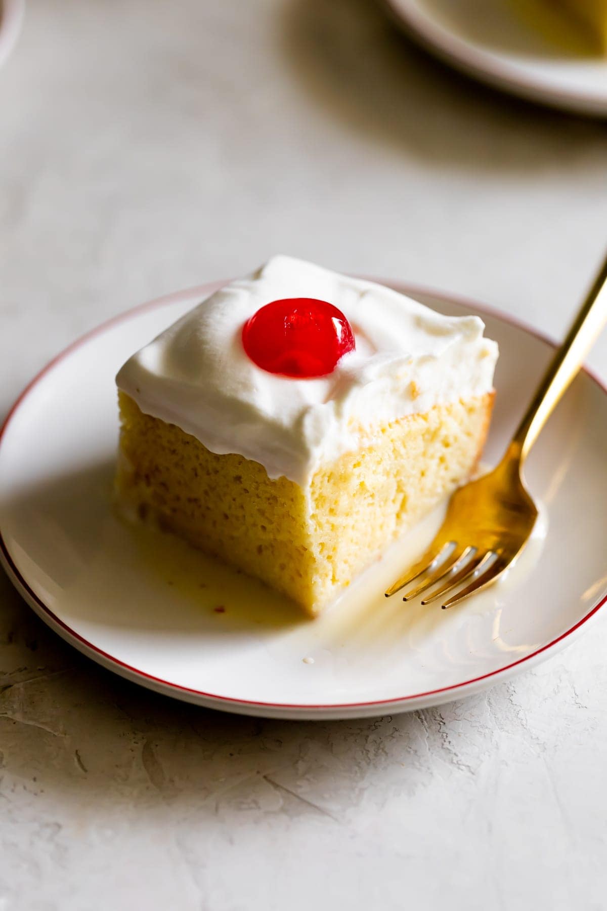 slice of tres leches cake with a cherry on top on a white plate on a white table